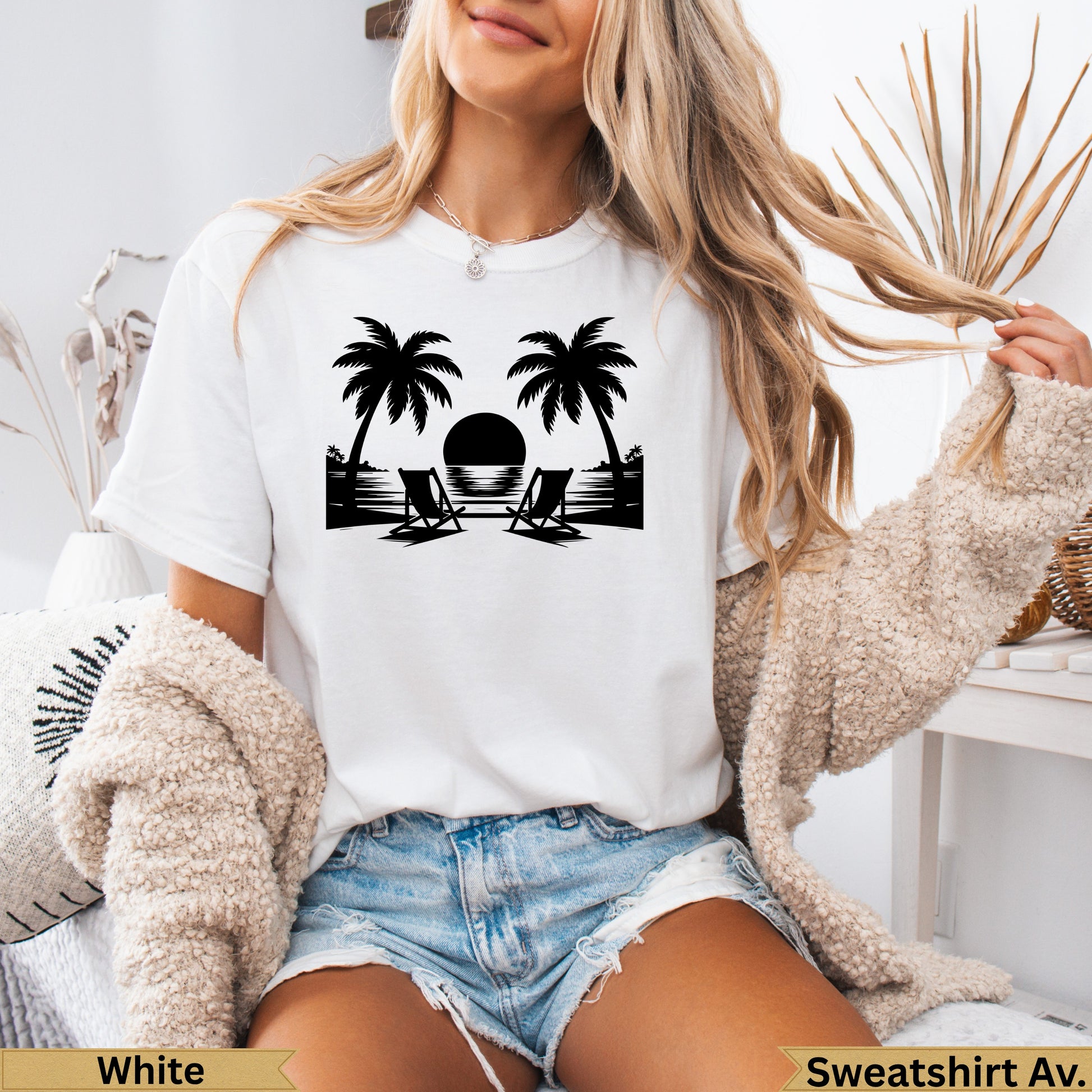 White t-shirt with black silhouette of palm trees, beach chairs, and sunset.