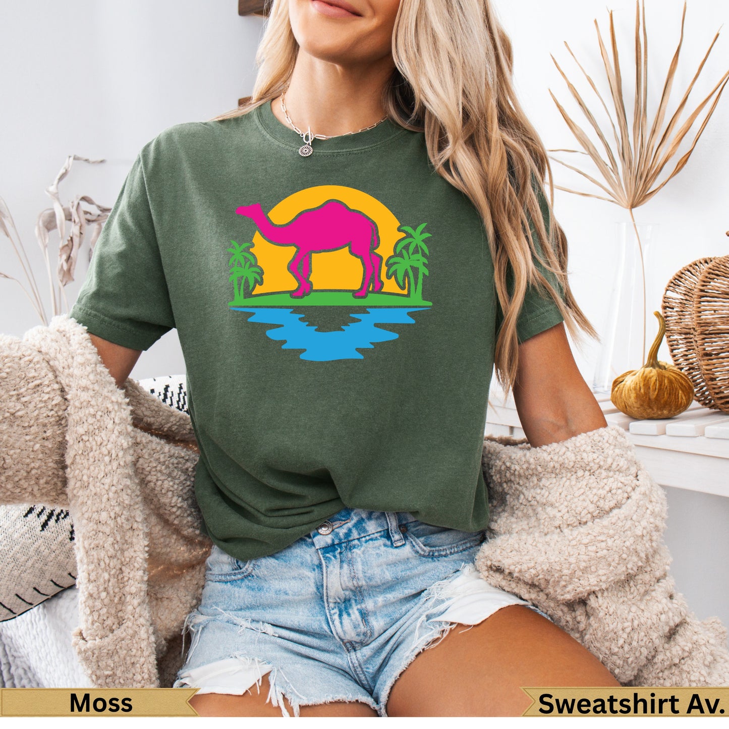 Olive green t-shirt with a neon pink camel silhouetted against a sunset and water scene.