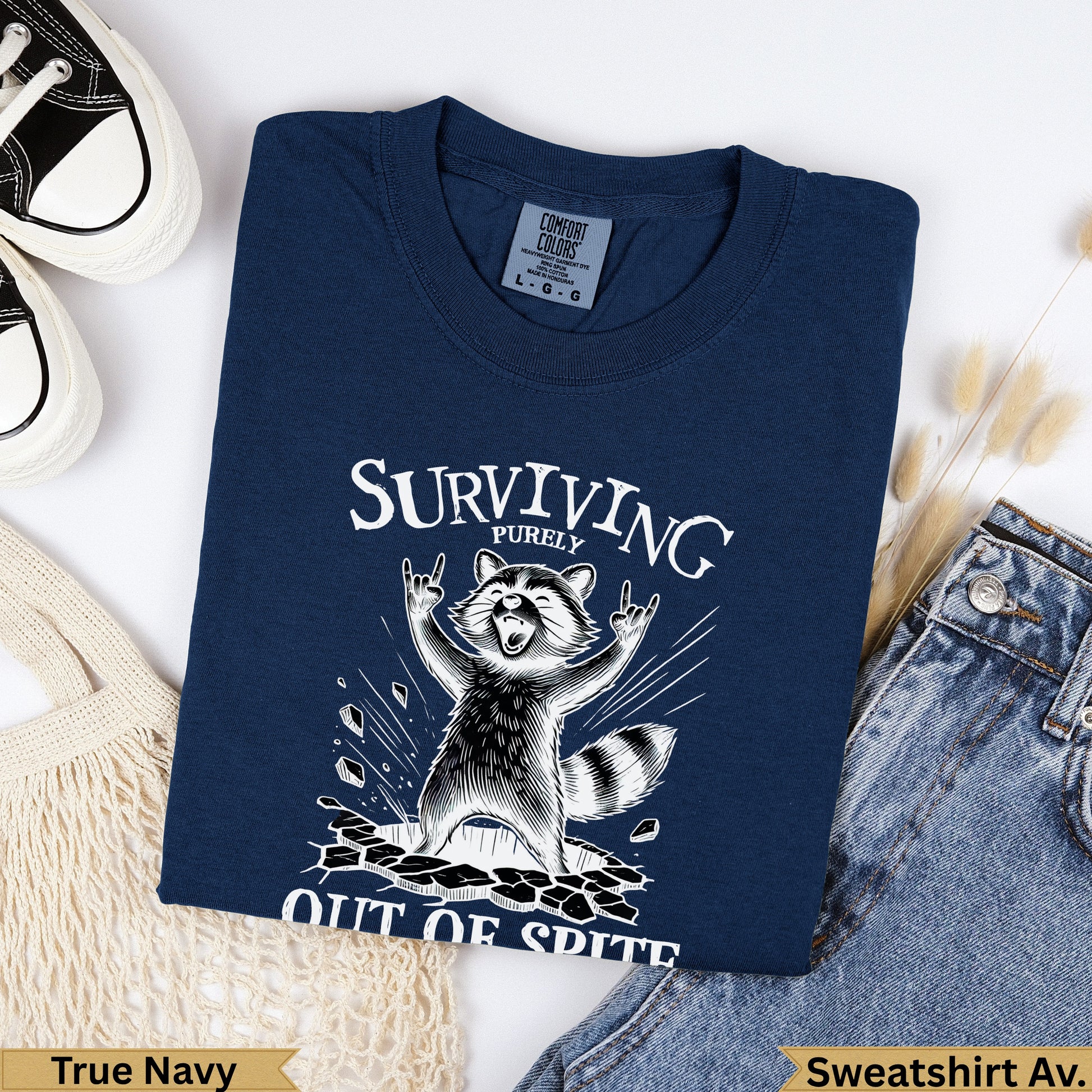 Navy Comfort Colors sweatshirt with raccoon graphic and "Surviving Purely Out of Spite" text.