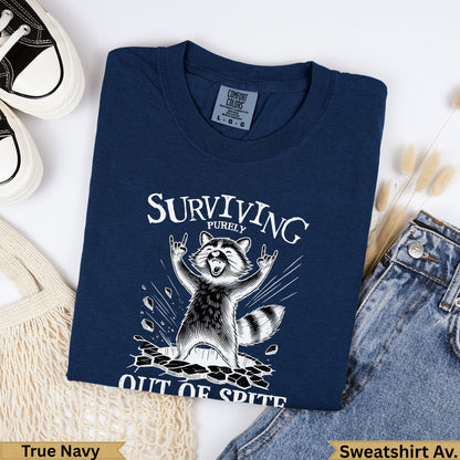 Navy Comfort Colors sweatshirt with raccoon graphic and "Surviving Purely Out of Spite" text.