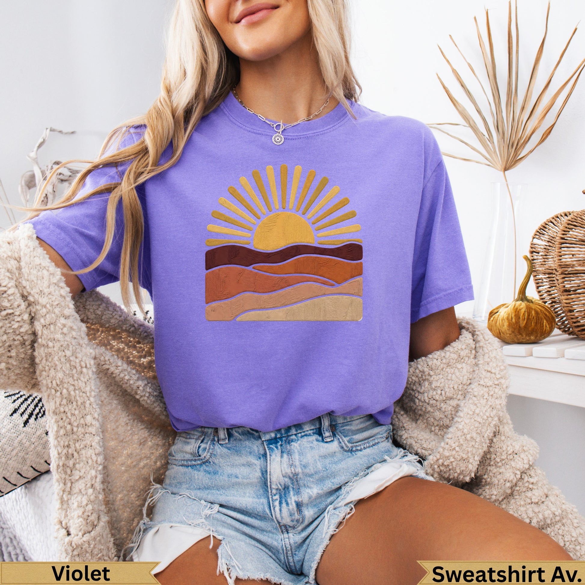 Purple t-shirt with a stylized sunrise over layered landscape.