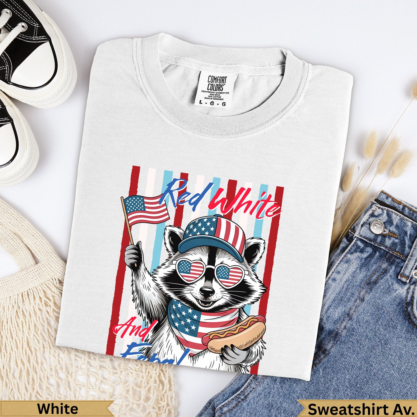 White Comfort Colors sweatshirt with raccoon in sunglasses holding American flag and hot dog.