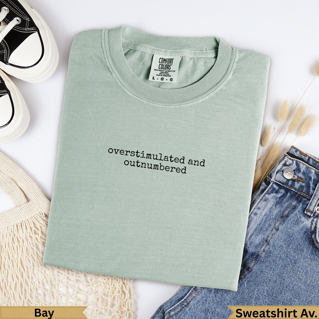 Light green Comfort Colors sweatshirt with "overstimulated and outnumbered" text.