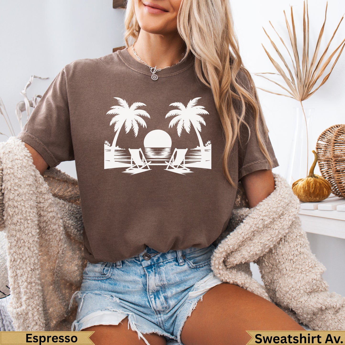 Brown t-shirt with silhouette of two palm trees, lounge chairs, and sun over ocean.