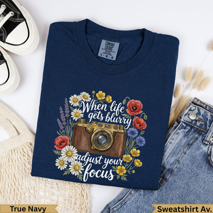Navy t-shirt with camera, flowers, and "When life gets blurry adjust your focus" text.