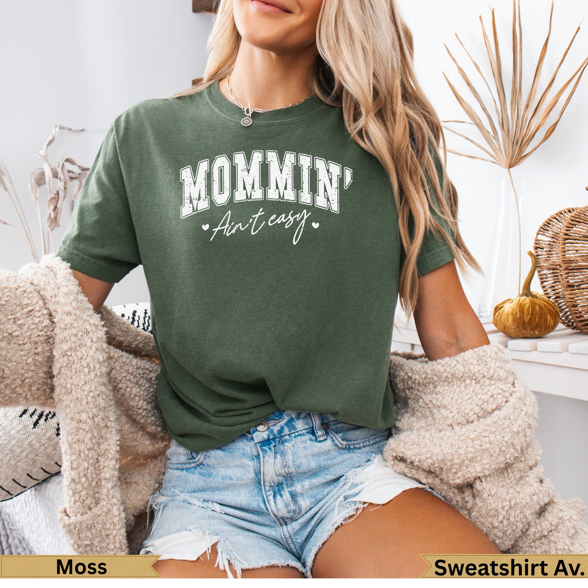 Green sweatshirt with "MOMMIN' Ain't Easy" text, worn by a woman.