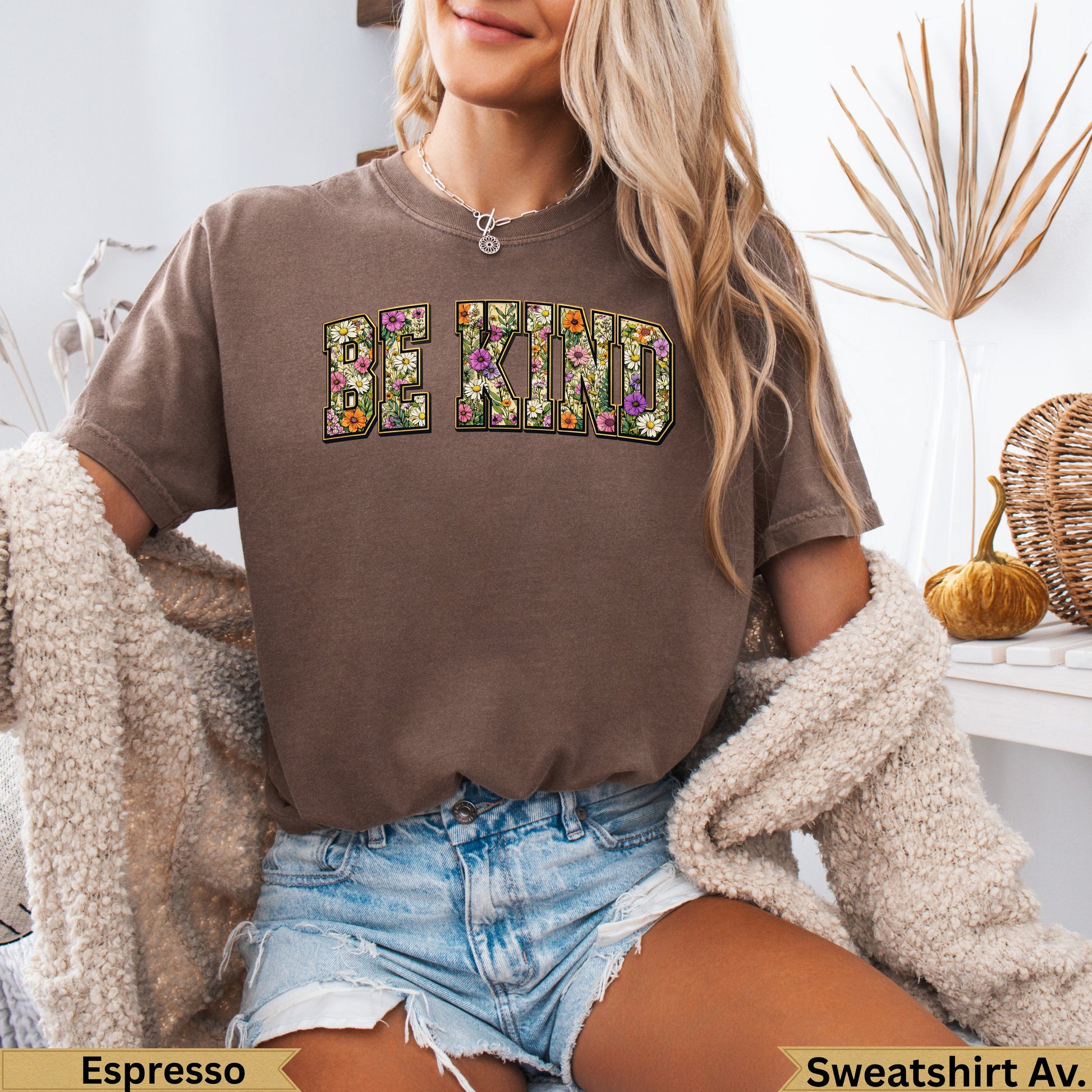 Brown t-shirt with "BE KIND" in floral letters, worn by a woman.