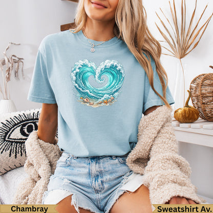Light blue t-shirt with heart-shaped wave graphic and seashells on sand.