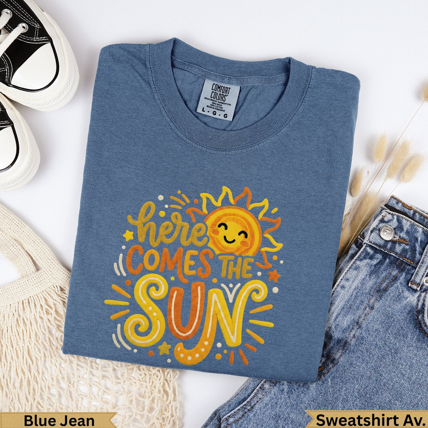 Blue t-shirt with "here comes the sun" graphic and smiling sun.