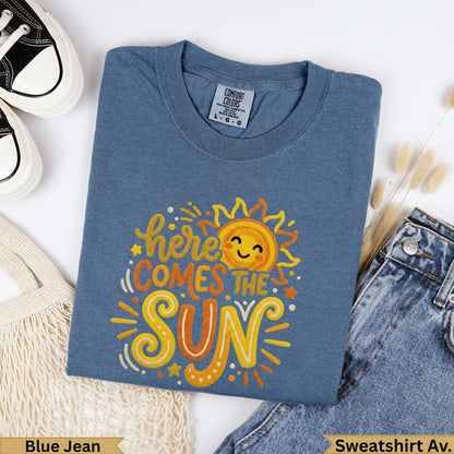 Blue t-shirt with "here comes the sun" graphic and smiling sun.