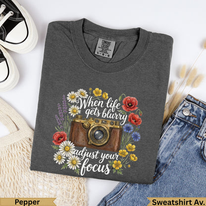 Dark gray t-shirt with a vintage camera and floral illustration, "When life gets blurry adjust your focus."