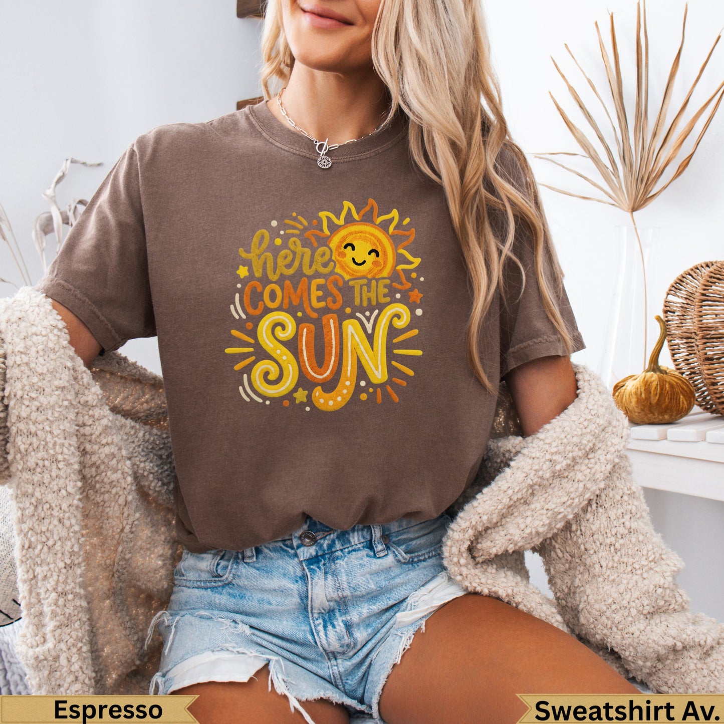 Brown sweatshirt with "here comes the sun" text and smiling sun graphic.