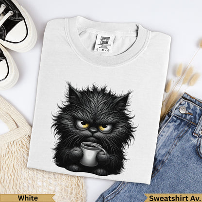 Fluffy black cat with yellow eyes holding a coffee mug on a white t-shirt.