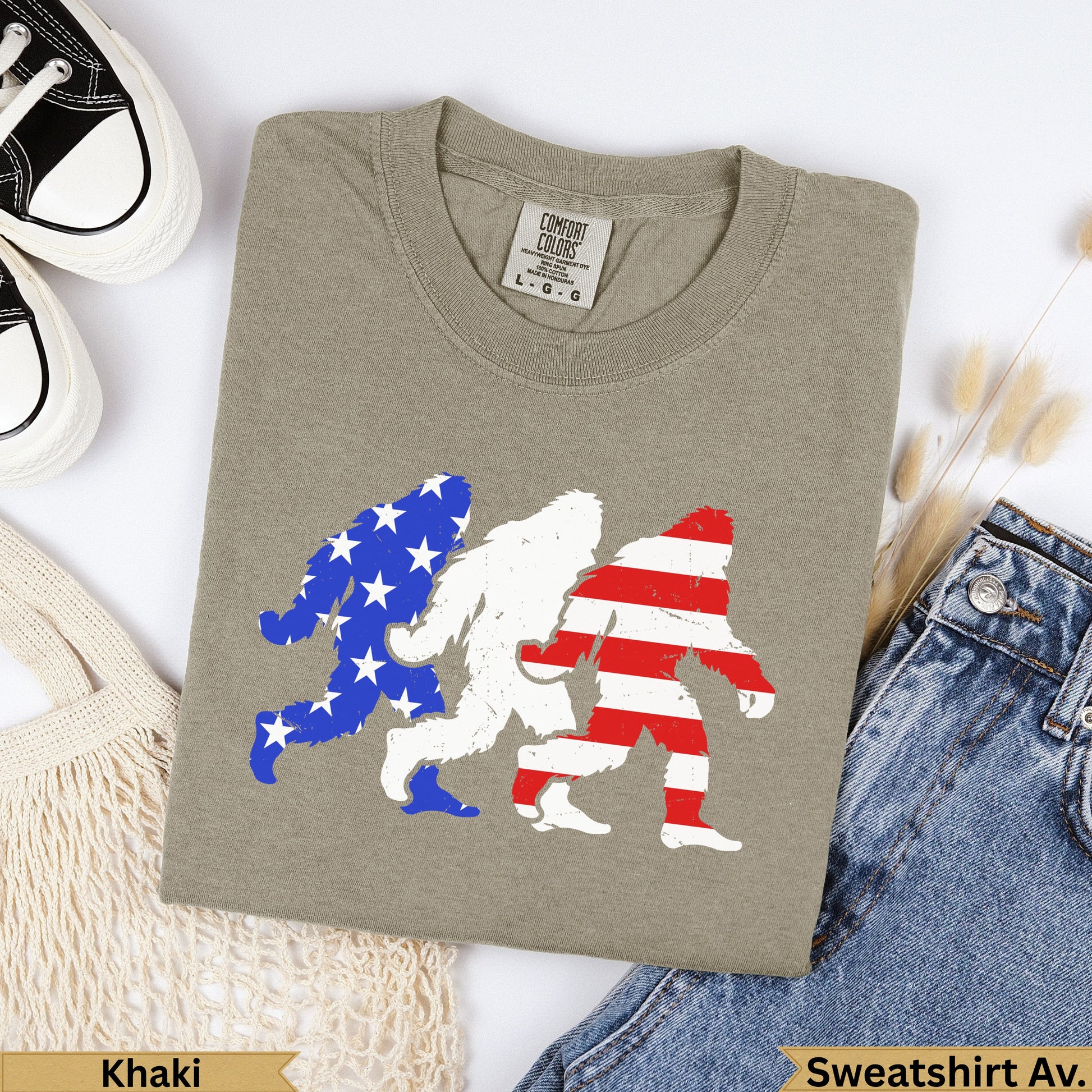 Three Bigfoot figures in US flag patterns on a khaki t-shirt.