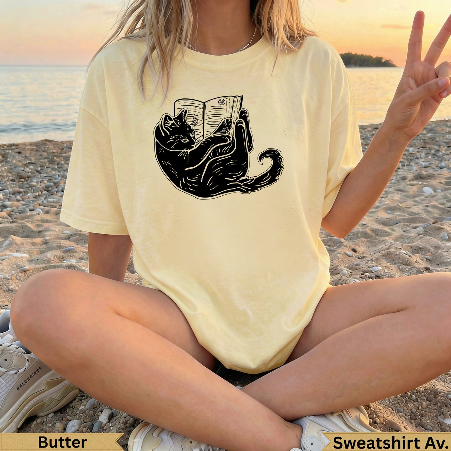 Black cat reading a book graphic on a light yellow t-shirt.