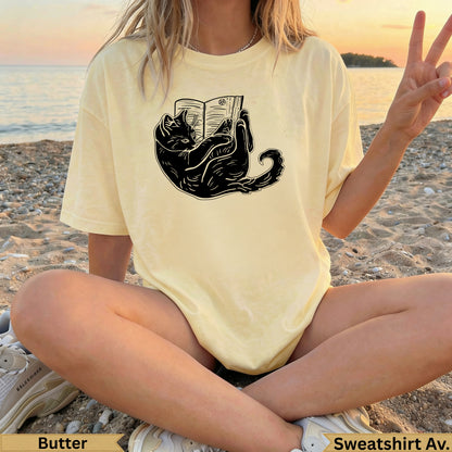 Black cat reading a book graphic on a light yellow t-shirt.