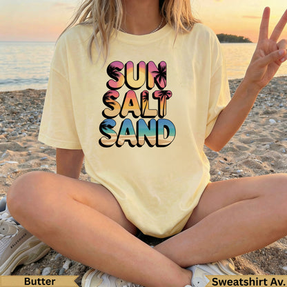 Yellow sweatshirt with "SUN SALT SAND" text and palm trees, worn by person on beach.