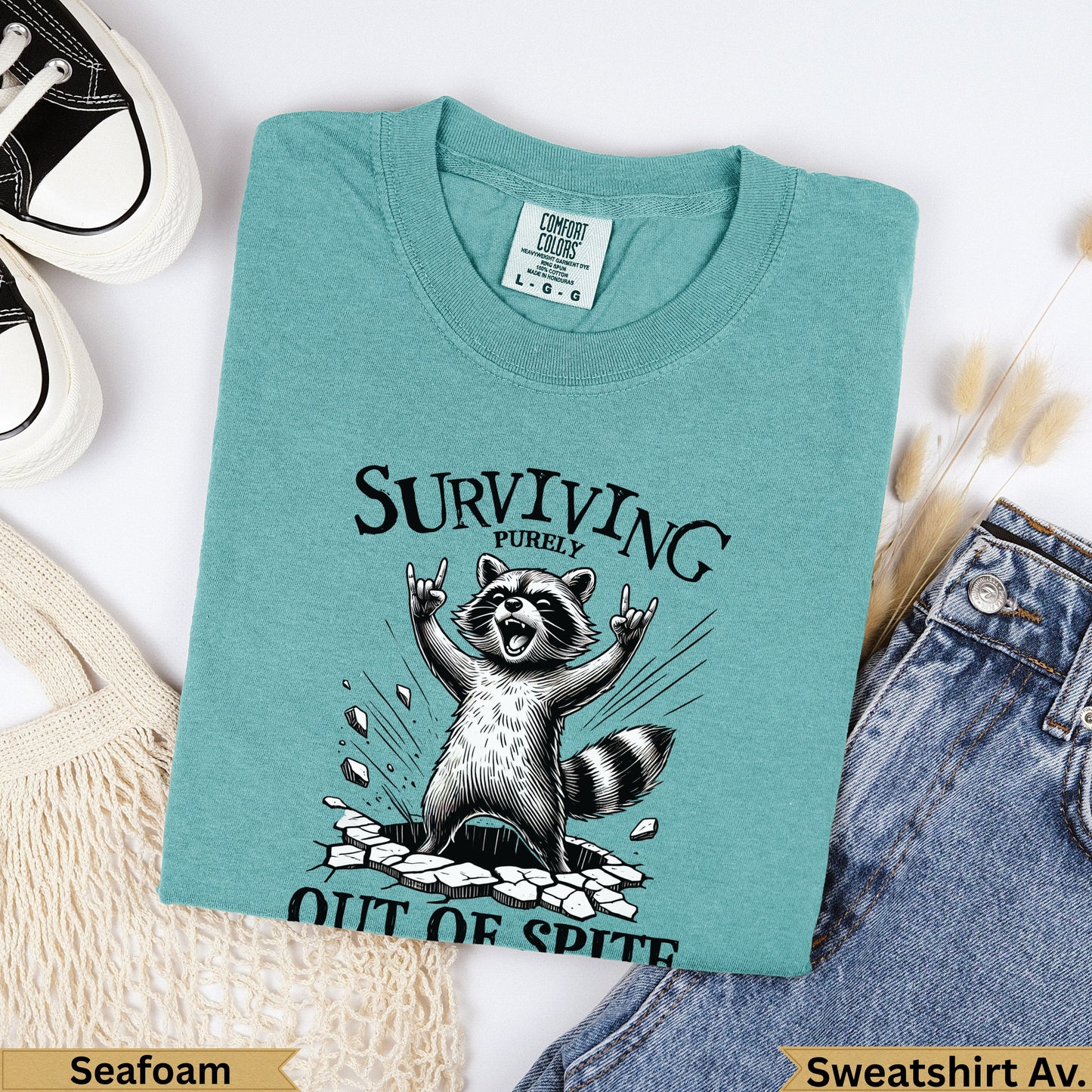 Seafoam t-shirt with raccoon celebrating "Surviving Purely Out of Spite."