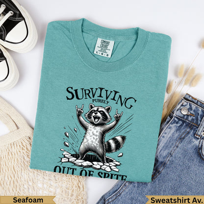 Seafoam t-shirt with raccoon celebrating "Surviving Purely Out of Spite."