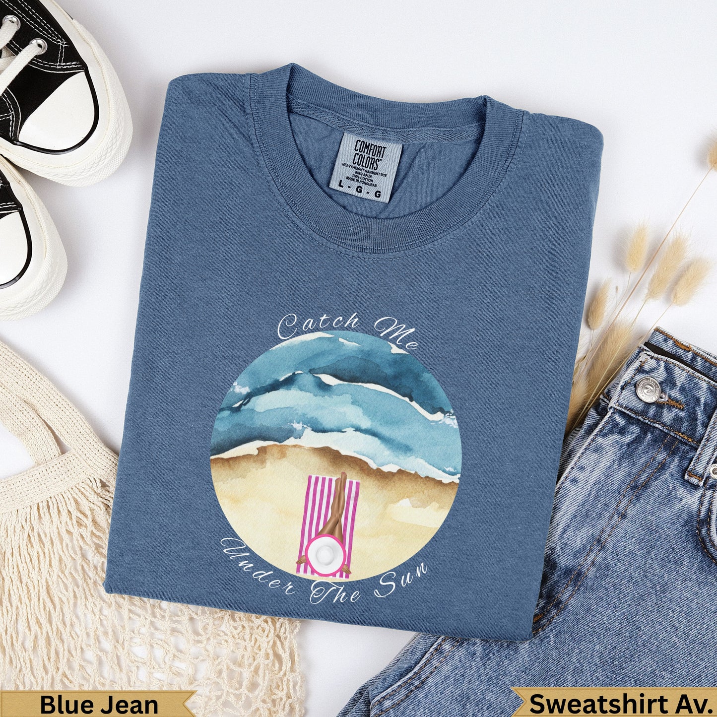 Blue t-shirt with "Catch Me Under The Sun" text and beach scene.