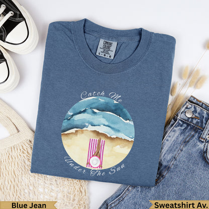 Blue t-shirt with "Catch Me Under The Sun" text and beach scene.
