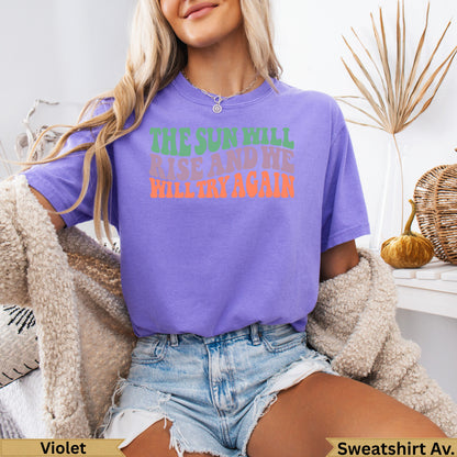 Purple t-shirt with "THE SUN WILL RISE AND I WILL TRY AGAIN" text.