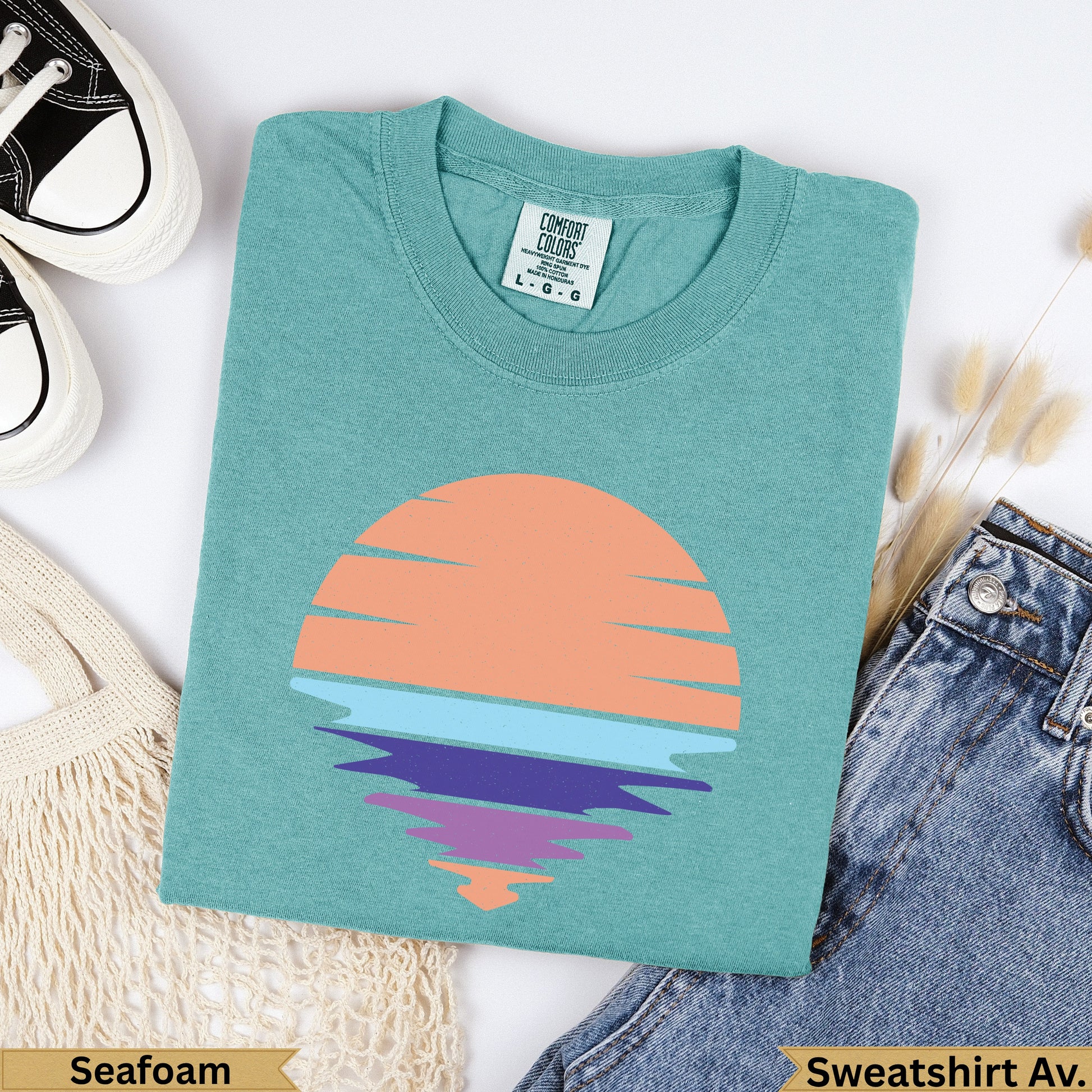Teal t-shirt with a retro sunset graphic, laid flat with jeans.