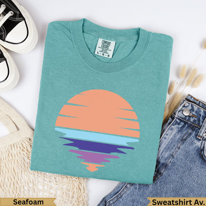 Teal t-shirt with a retro sunset graphic, laid flat with jeans.