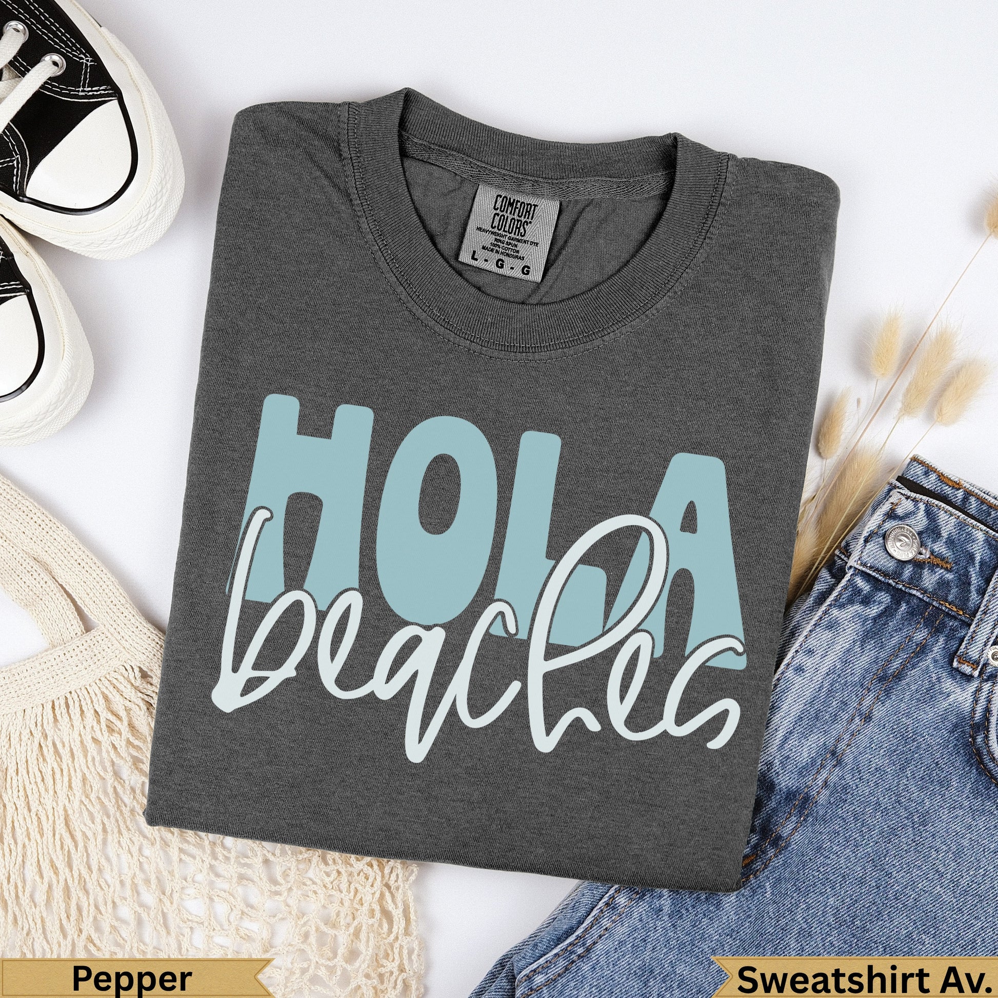 Dark grey Comfort Colors sweatshirt with "Hola beaches" in light blue text.