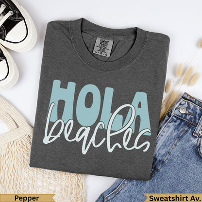 Dark grey Comfort Colors sweatshirt with "Hola beaches" in light blue text.