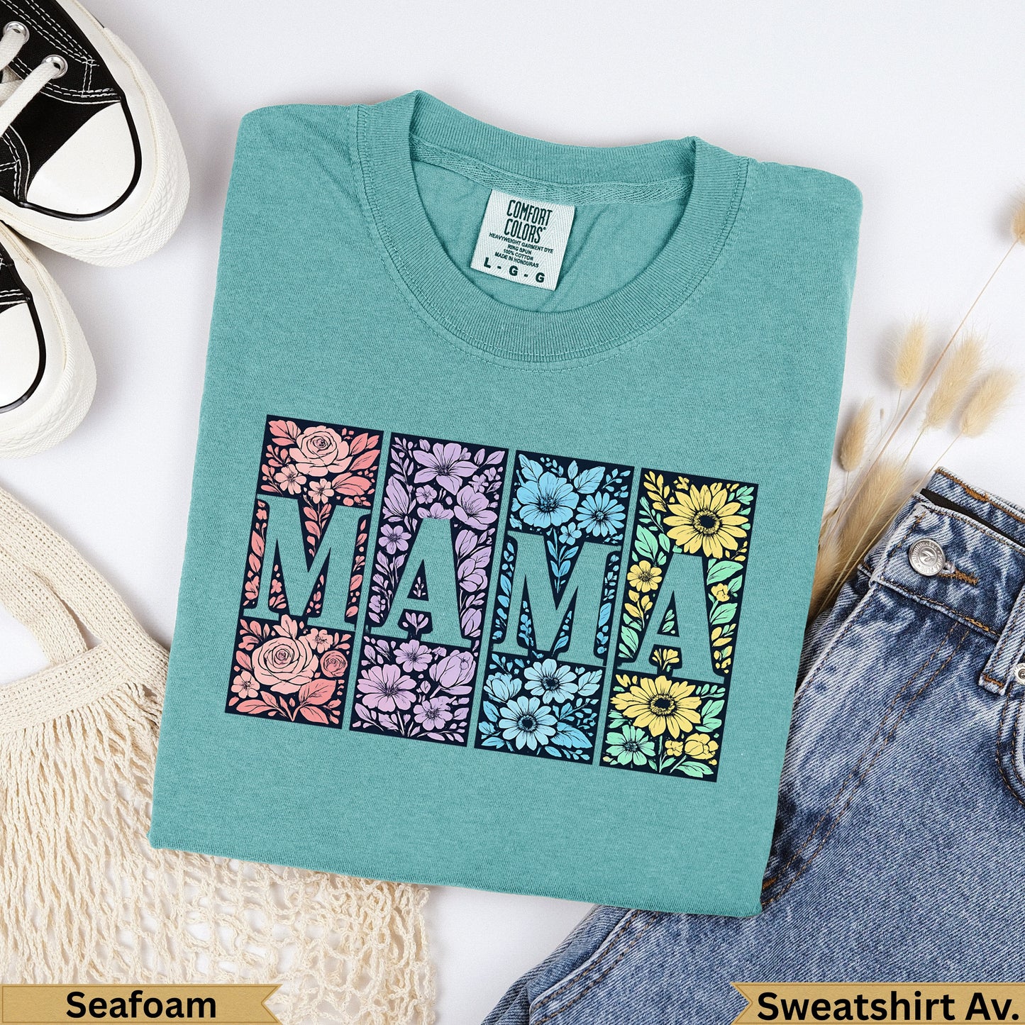Teal t-shirt with "MAMA" in floral blocks, against a background of jeans and a bag.