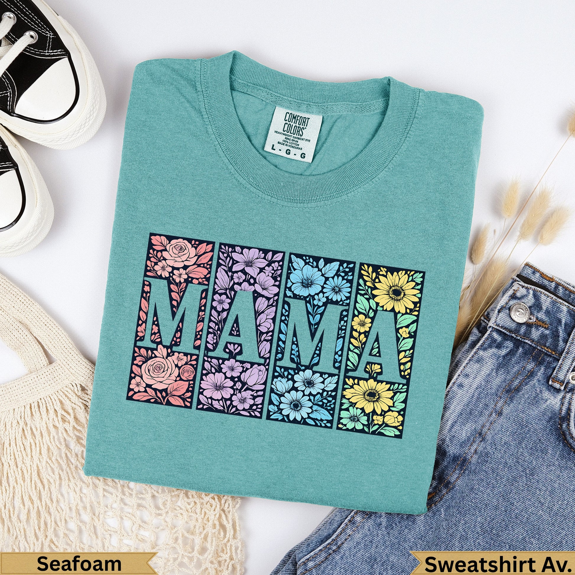 Teal t-shirt with "MAMA" in floral blocks, against a background of jeans and a bag.