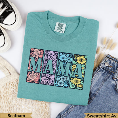 Teal t-shirt with "MAMA" in floral blocks, against a background of jeans and a bag.