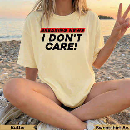Yellow t-shirt with "BREAKING NEWS I DON'T CARE!" text, worn by a person sitting on a beach.