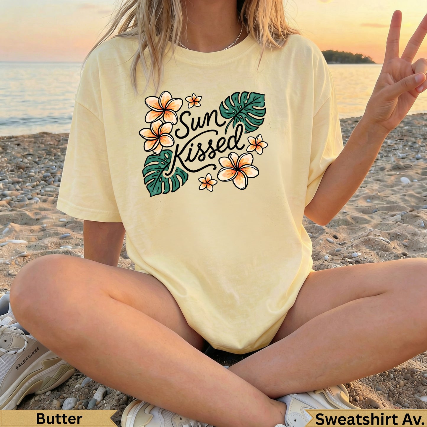 Light yellow t-shirt with "Sun Kissed" and floral graphic, woman sitting on beach.