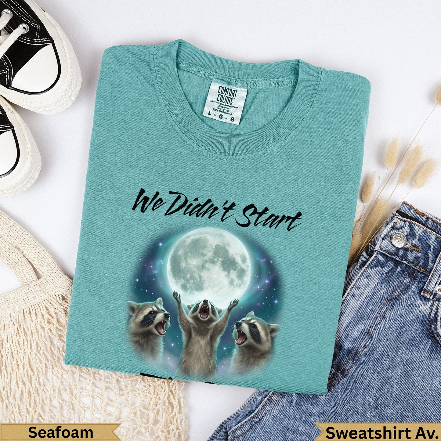 Teal sweatshirt with three raccoons howling at a full moon and the text "We Didn't Start".